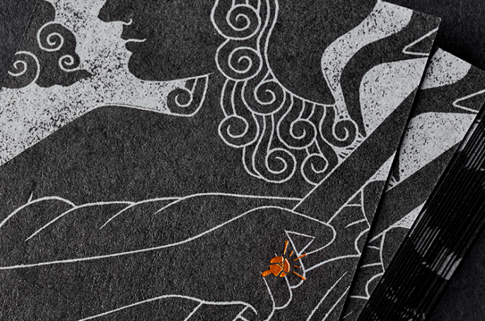 Close-up of an illustration on the back of a business card depicting a Greek goddess wearing a bronze coloured ring