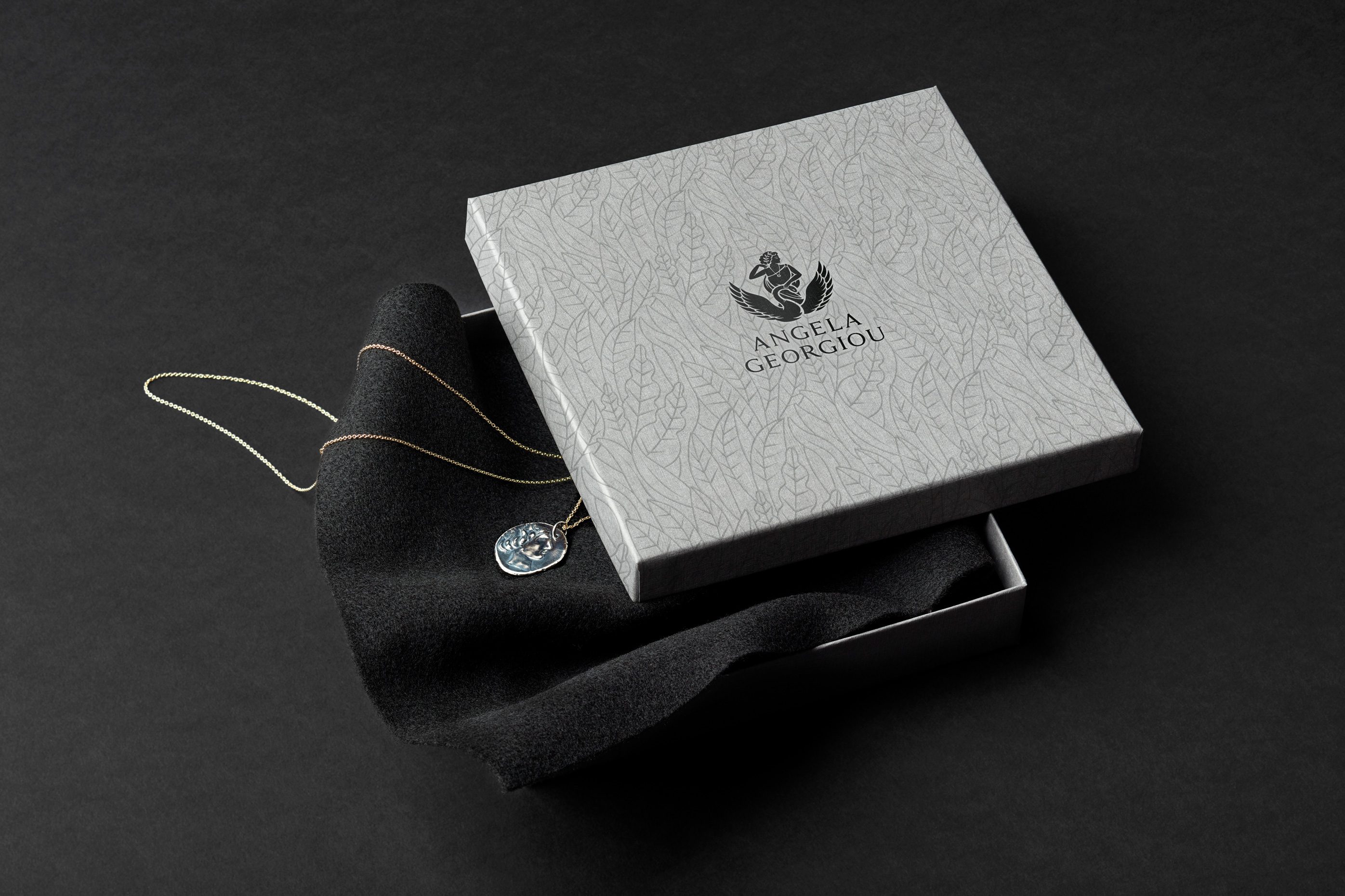 Open branded jewellery box against a dark background showing detailed design and logo to front lid