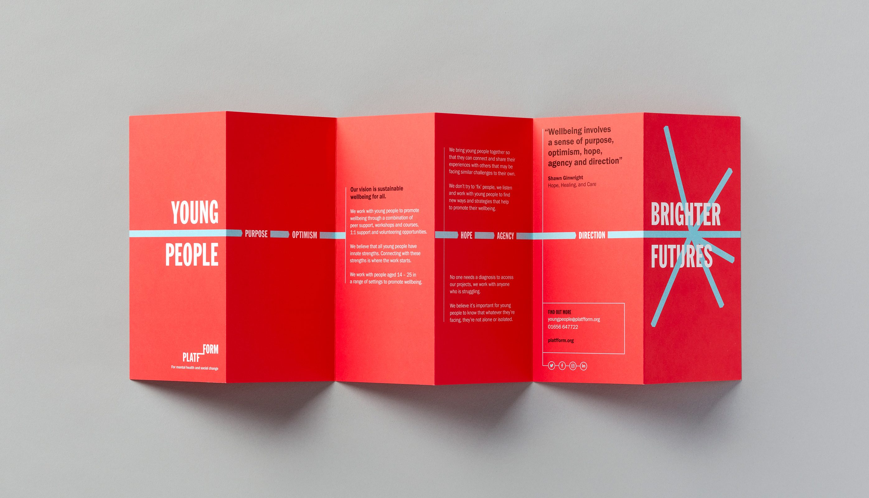 Red coloured concertina folded leaflet laying open and showing design against grey background