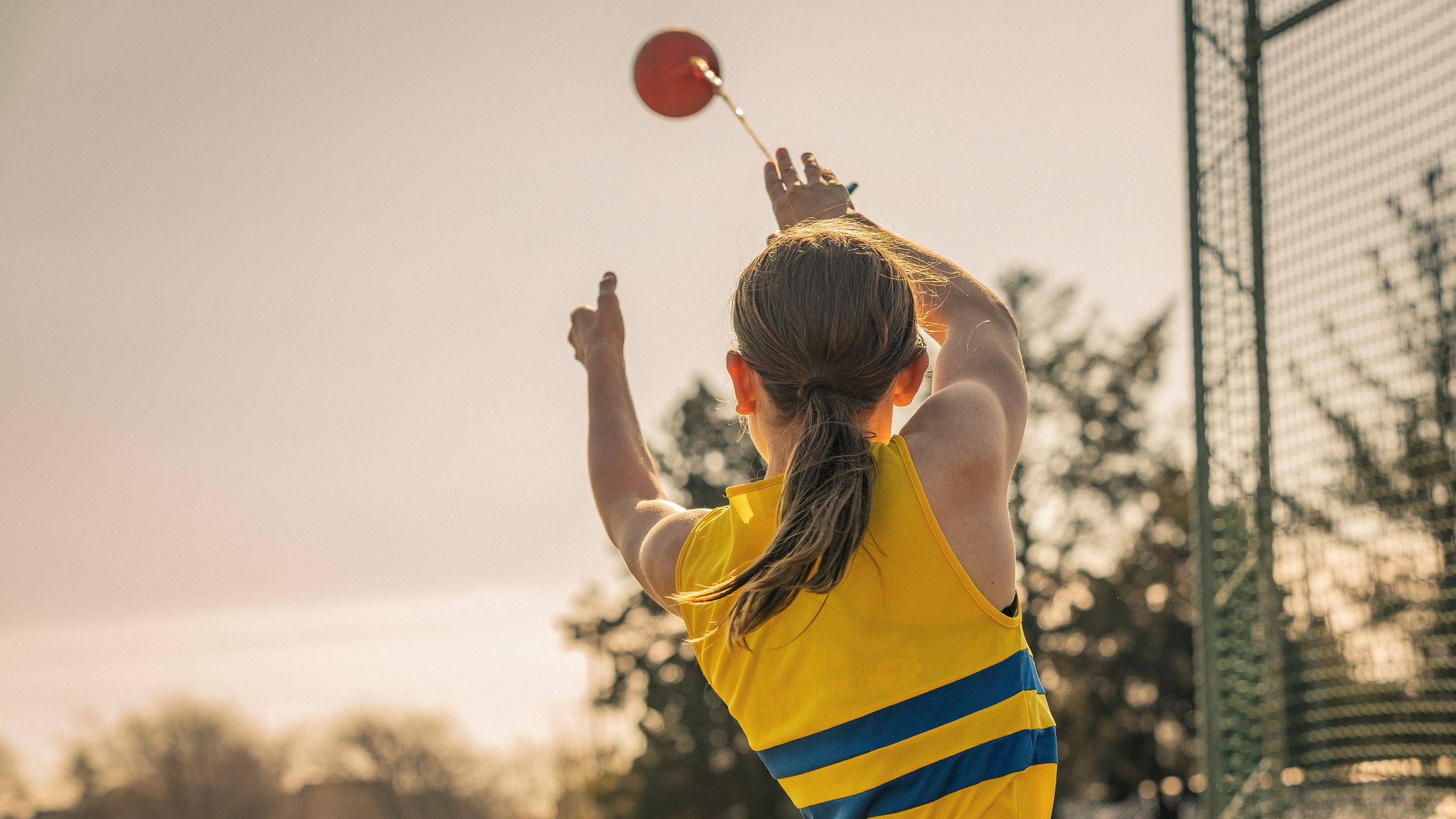 Female junior athlete throwing shot put wearing branded athletics club vest