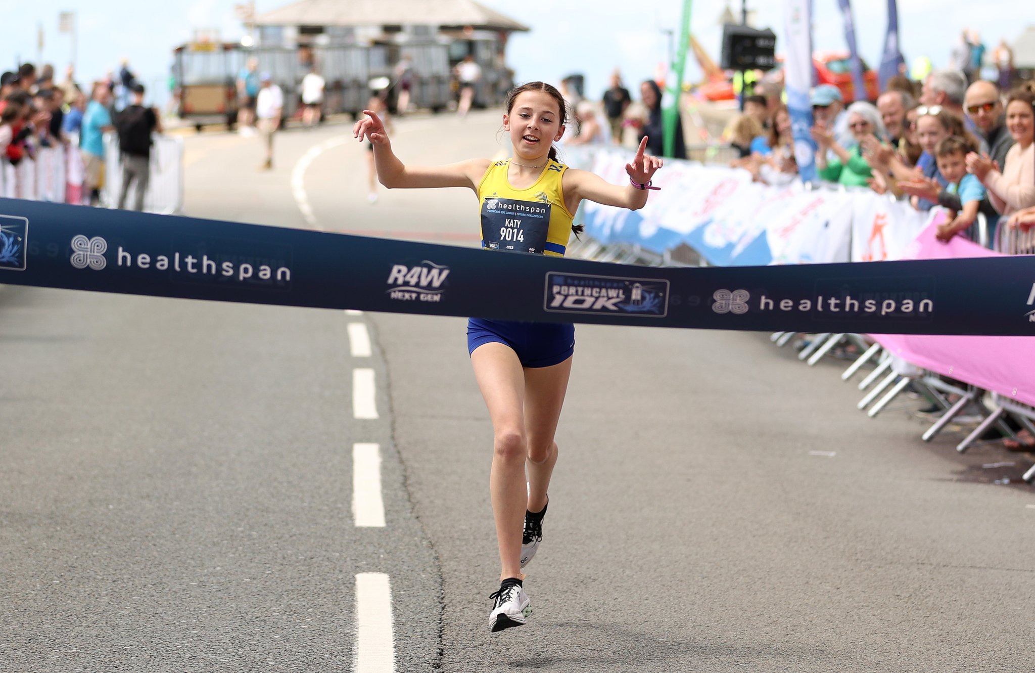 Junior female athlete crossing finish line of 10k race wearing branded club vest