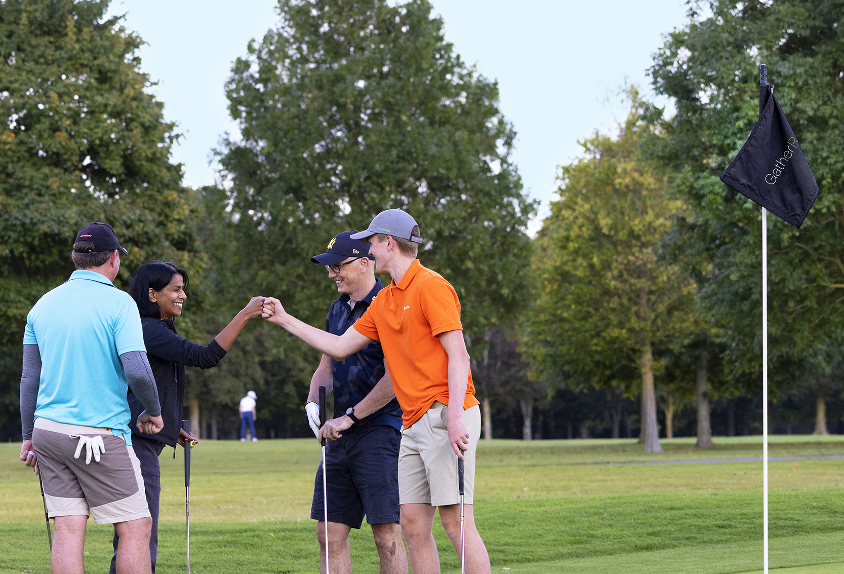 Four people doing a fist pump on golf course alongside event branded flag