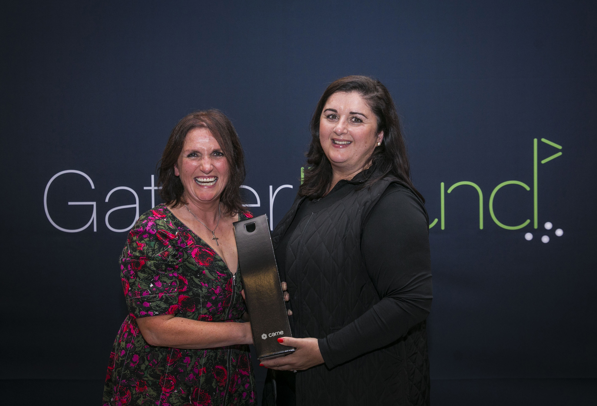 Two women golfers receiving prize against branded golf event backdrop